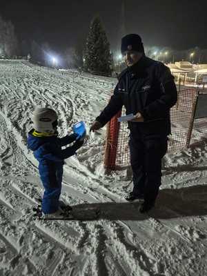 Zdjęcie przedstawiające funkcjonariusza Policji, który przekazuje ulotkę informacyjną