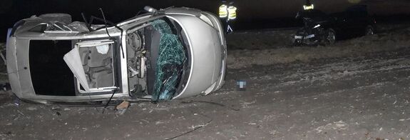 Zdjęcie przedstawiające dwa pojazdy biorące udział w zdarzeniu drogowym. W tle widoczni policjanci w kamizelkach odblaskowych.