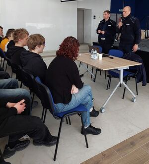 Zdjęcie przedstawiające dwóch funkcjonariuszy prowadzących spotkanie z młodzieżą szkolną