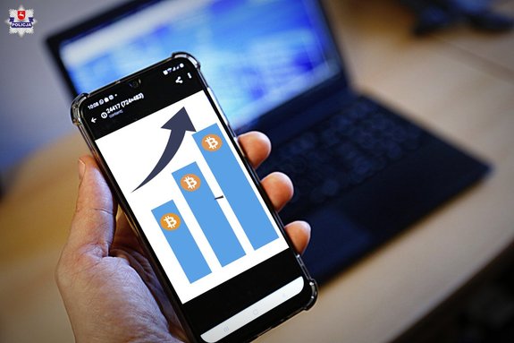 Telefon komórkowy w dłoni, w tle laptop.