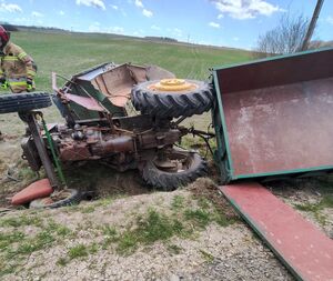 Leżący na boku rozbity ciągnik rolniczy z przyczepą