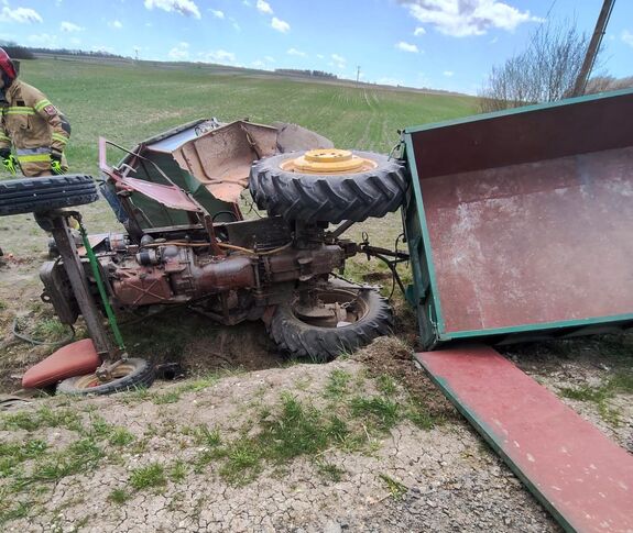 Leżący na boku rozbity ciągnik rolniczy z przyczepą