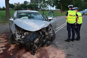 Stojący na jezdni samochód z uszkodzonym przodem, a obok niego dwie policjantki.