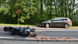 Samochód z uszkodzonym przodem i leżący na jezdni motocykl.