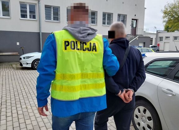 Policjant prowadzi zatrzymanego mężczyznę.