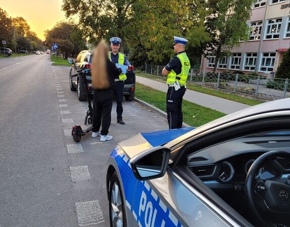 Policjanci przekazują kask ochronny dziewczynie na hulajnodze elektrycznej.