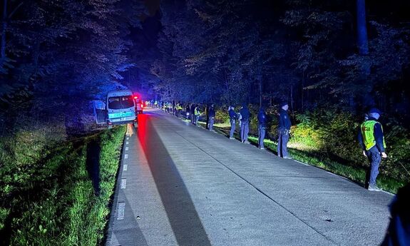 Policjanci stoją wzdłuż lasu.