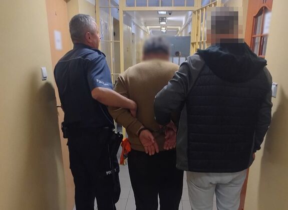 Policjanci prowadzą zatrzymanego mężczyznę.