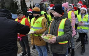 Grupa dzieci z koszyczkiem jabłek i talerzem cytryn i stojący tyłem mężczyzna sięgający po cytrynę