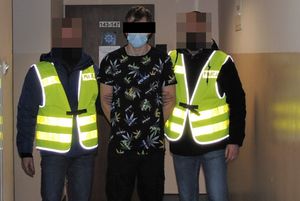 policjanci prowadzą zatrzymanego młodego mężczyznę.